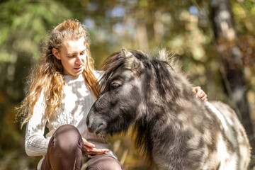 A young woman and her shetland pony cuddle together in a forest in autumn outdoors