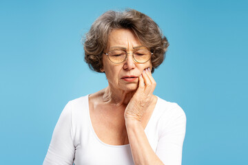 Portrait of upset mature senior  woman wearing eyeglasses touching face having toothache isolated...