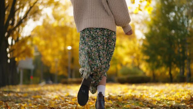 back view stunning young brunette woman joyfully running in autumn park with yellow foliage. happy attractive girl in retro casual wear walks in park at warm fall day. slow motion 4k footage