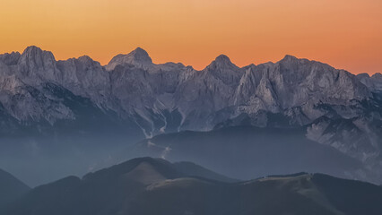 Panoramic sunrise view from summit Dobratsch on Julian Alps and Karawanks in Austria, Europe. Silhouette of endless mountain ranges with orange and pink colors of sky. Jagged sharp peaks and valleys