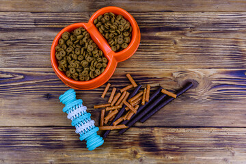 Bowl with pet food, dog toy  for teeth cleaning and dog treats on a wooden background. Top view