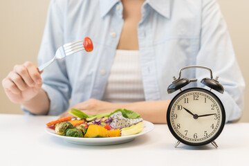 Intermittent fasting with clock, close up young woman, girl diet, waiting time to eat ketogenic low carb, green vegetable salad on plate. Eat food healthy first meal on brunch, lunch on table at home.
