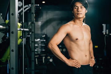 Fototapeta na wymiar Athletic Asian man with a positive attitude, standing on his waist and looking at his trainer, works hard to build his strength and achieve his fitness goals. Healthy fitness Lifestyle with copy space