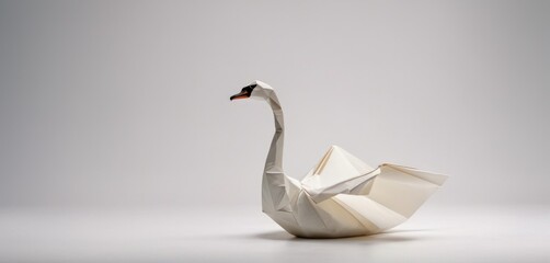  a white origami swan sitting on top of a white table next to a black object with a red beak.