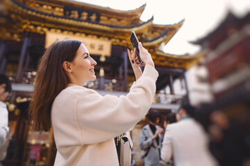 brunette girl taking photos on her phone of a pagoda in Yuyuan