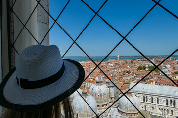 Tourist woman wearing hat with aerial view from St Mark bell tower Campanile of old town Venice, Veneto, Italy, Europe. Looking at Santa Maria Della Salute, Venetian lagoon. UNESCO World Heritage - obrazy, fototapety, plakaty