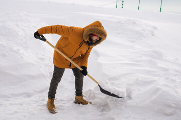 Young man clearing snow in his backyard village house with shovel. Remove snow from the sidewalk.