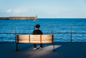 un adolescent assis sur un banc face à la mer méditerranée. Jeune migrant regardant la mer....