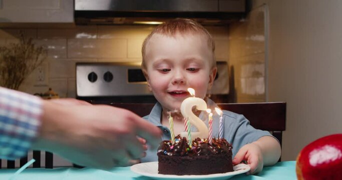 Baby boy blowing out candles on cake while family celebrates his birthday home