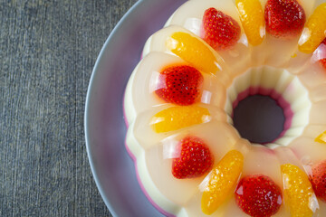 puding lapis or layer pudding with orange and strawberry slices served on a plate at the dark table. has a soft texture and tastes fresh. healthy food. top view