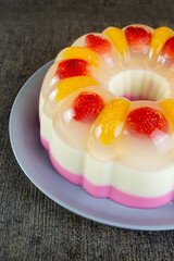 puding lapis or layer pudding with orange and strawberry slices served on a plate at the dark table. has a soft texture and tastes fresh. healthy food