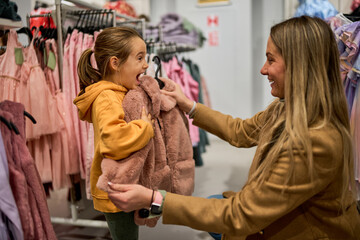 The mom shows her daughter a piece of clothing she wants to buy, pressing it against her to check...