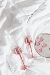 Pink shining champagne glasses and burning candles as hearts on bed cloth. Lifestyle aesthetic...