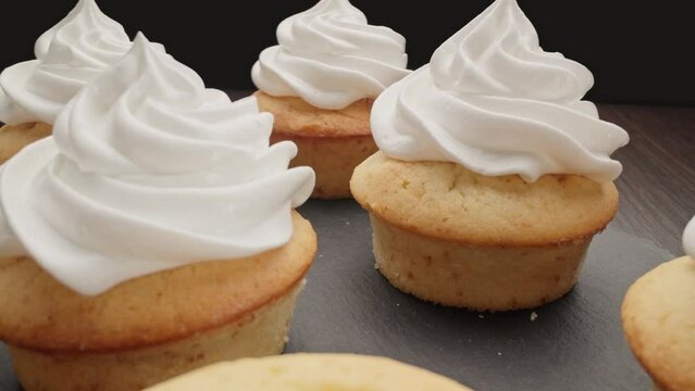 Decorating cupcake with white cream. Cooking delicious homemade cakes. Home bakery concept. Decorating muffins with cream. Dolly shot using laowa probe lens. Close-up in 4K, UHD