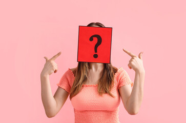 Young woman pointing at paper sheet with question mark on pink background