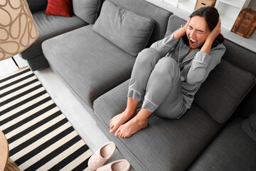 Beautiful young afraid woman sitting on sofa and screaming in living room