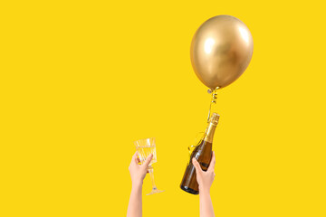 Female hands with balloon, glass and bottle of champagne on yellow background © Pixel-Shot