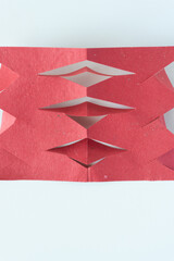 folded and cut red paper object with triangle tabs on white