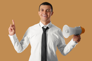 Young businessman with megaphone pointing at something on brown background