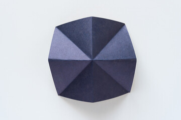 cut and folded indigo paper shape with crease lines (radial pattern) on blank paper