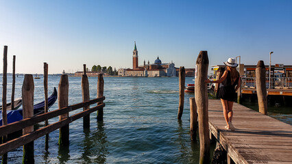 Tourist woman on wooden fotsteg with scenic view of San Giorgio di Maggiore island in Venice, Veneto, Northern Italy, Europe. Gondolas moored by Saint Mark square, Venetian Lagoon. Tranquil atmosphere © Chris