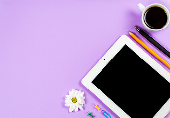 Stationery items, a cup of coffee and a tablet on a purple background, office
