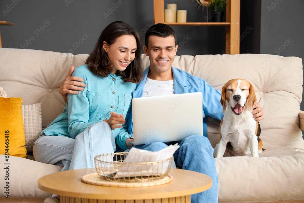 Poster young couple with cute beagle dog and laptop on sofa at home