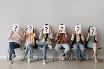 Applicants holding paper sheets with question marks near light wall