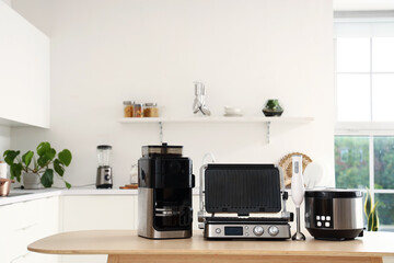 Wooden table with set of modern appliances in light kitchen - obrazy, fototapety, plakaty