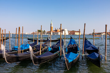 Group of gondolas moored by Saint Mark square in city of Venice, Veneto, Northern Italy, Europe. Scenic view of San Giorgio di Maggiore church in background. Romantic vacation in the Venetian Lagoon - obrazy, fototapety, plakaty