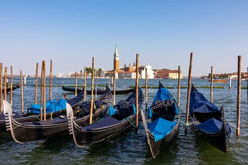 Poster Group of gondolas moored by Saint Mark square in city of Venice, Veneto, Northern Italy, Europe. Scenic view of San Giorgio di Maggiore church in background. Romantic vacation in the Venetian Lagoon © Chris