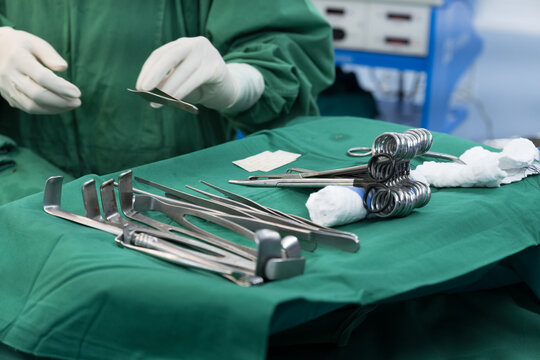 Surgeon doctor's hand with hygiene glove taking surgical clamps and medical equipment on green surgical tray inside operating room.Sterile surgical instrument tool equipment for surgery.