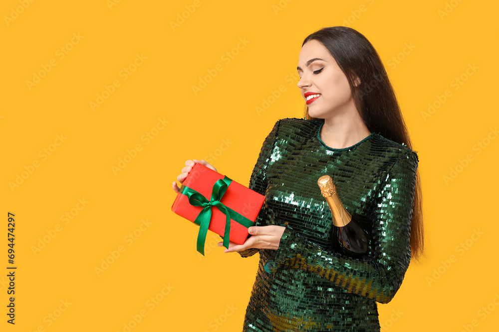 Canvas Prints Beautiful young woman with bottle of champagne and Christmas gift on yellow background