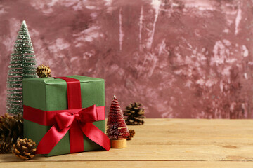 Christmas gift box with pine cones and decorative trees on wooden table near pink grunge background