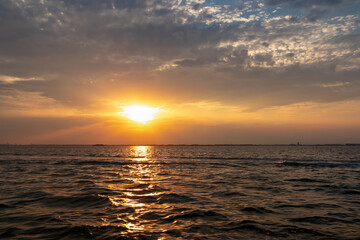 Scenic sunset view over Venetian lagoon seen from a boat in city of Venice, Veneto, Northern Italy, Europe. Reflection in the water creating romantic atmosphere. Orange red sky. Silhoutte of landmarks