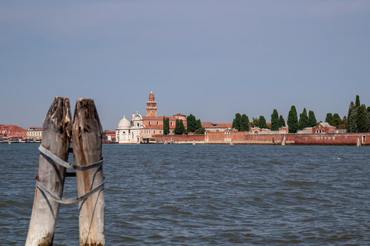 Panoramic view from the ferry to the island of Murano, Venice, Veneto, Italy, Europe. Summer tourism in Venetian lagoon in Adriatic sea. Timber piles indicating waterways. Famous landmarks in distance