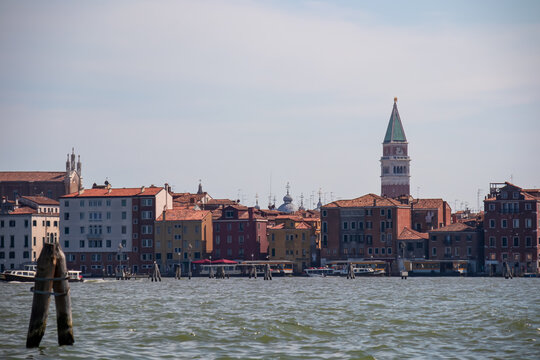 Scenic view from ferry of bell tower St Mark's Campanile, Venice, Veneto, Italy, Europe. Summer tourism in Venetian lagoon, Adriatic sea. Timber piles indicating waterway. Boat trip. Old town center