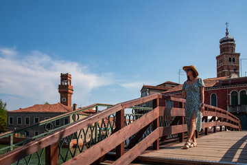 Tourist woman standing on San Pietro Martire bridge on Murano island in city of Venice, Veneto, Northern Italy, Europe. Venetian architectural landmarks. Boats on the water. Summer city tourism