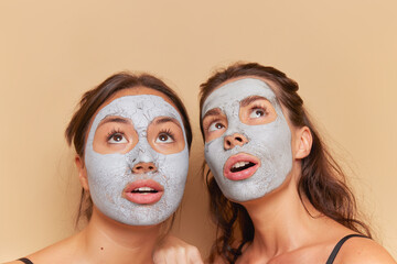 Two girls wearing makeup masks posing on background, looking up in surprise, healthcare products concept, copy space