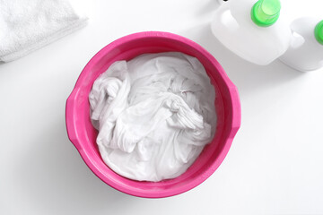 Basin with water, laundry and detergent on white table, top view