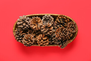 Wicker bowl with pine cones on red background