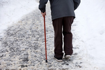 Elderly man with walking cane on a winter street. Concept of limping, old age, snow weather