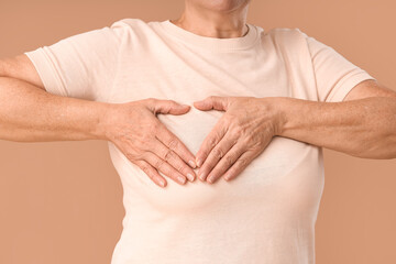 Mature woman checking her breast on brown background, closeup. Cancer awareness concept