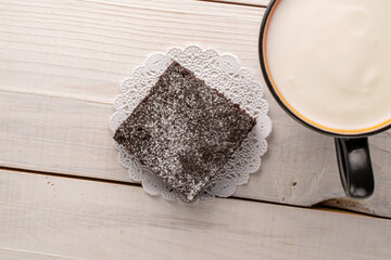 One piece of classic chocolate brownie with ceramic cup with sour cream on wooden table, macro, top view.