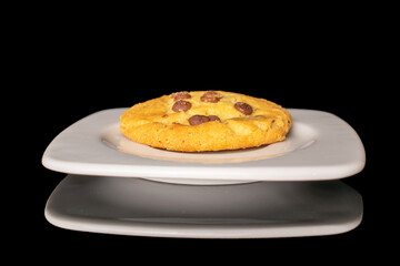 One classic chocolate chip cookie on white ceramic saucer, macro, isolated on black background.