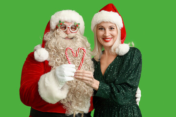 Santa Claus and beautiful mature woman in Christmas hats with candy canes on green background