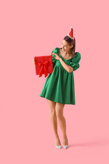 Beautiful woman in Santa hat with Christmas gift on pink background