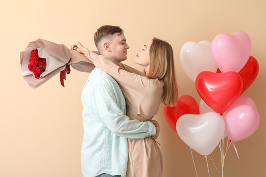 Lovely couple with bouquet of flowers and heart-shaped balloons on beige background. Valentine's Day celebration