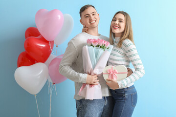 Lovely couple with bouquet of flowers, gift box and heart-shaped balloons on blue background....
