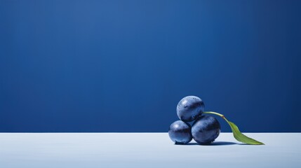  a group of three blue plums sitting on top of a table next to a green leaf on a blue background.